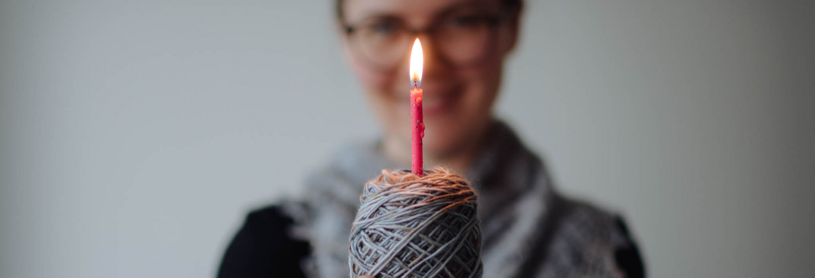 A white woman holds a cake of yarn with a lit birthday candle in it.